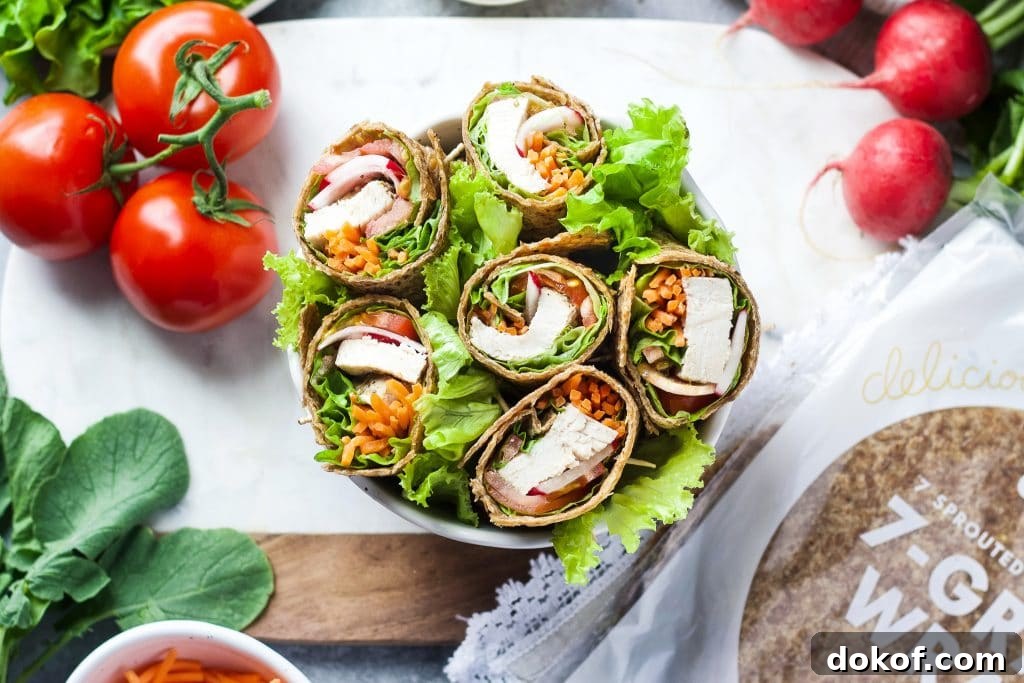 Chicken Caesar Wrap Recipe: Quick Protein-Packed Lunch 9 Healthy chicken Caesar wraps sitting in a bowl with radishes, tomatoes, lettuce, Caesar dressing, and extra wraps around it.