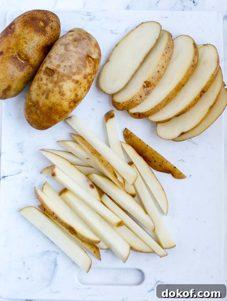 Potatoes cut to the shape of french fries on a cutting board.