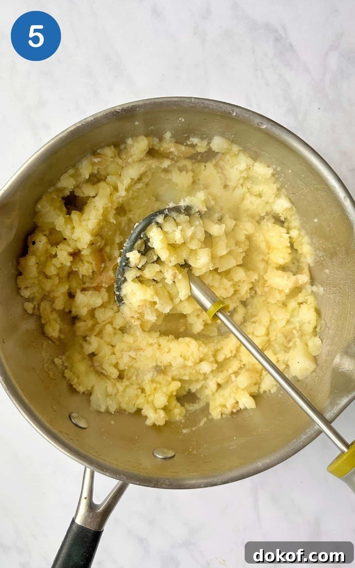 mashed potatoes in a saucepan with a potato masher.