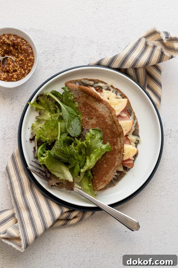 A crepe on a plate stuffed with ham, cheese and apples, with a salad alongside.