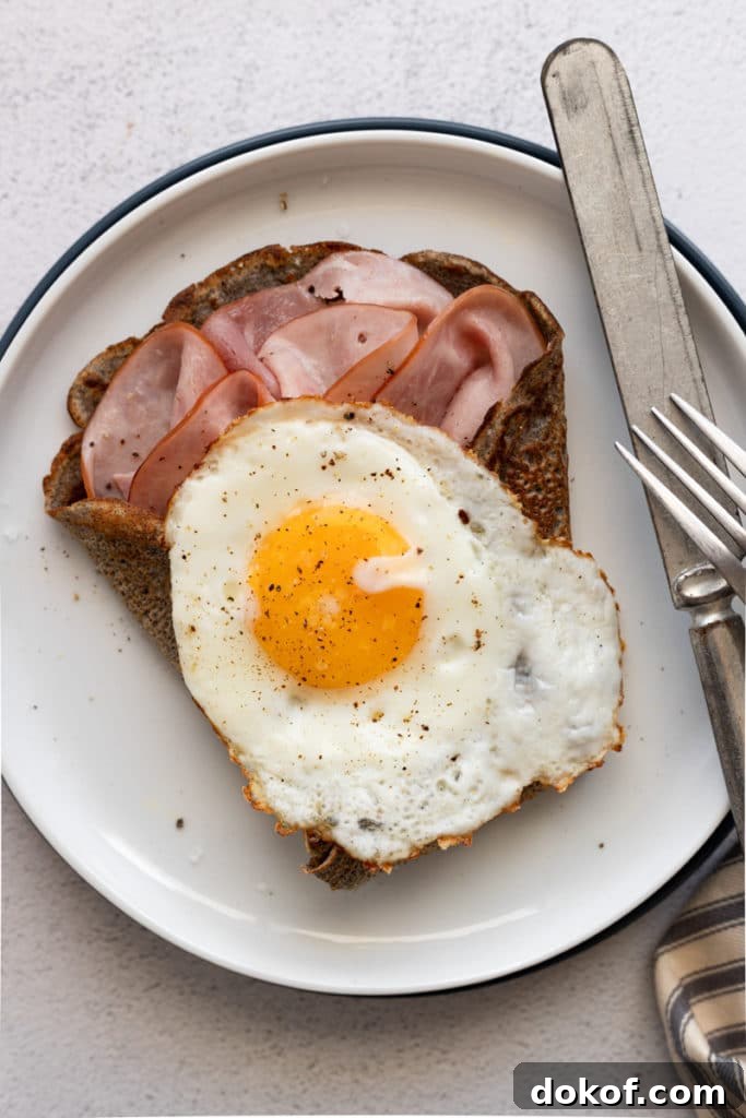 Close up of a crepe stuffed with sliced ham and topped with a fried egg.