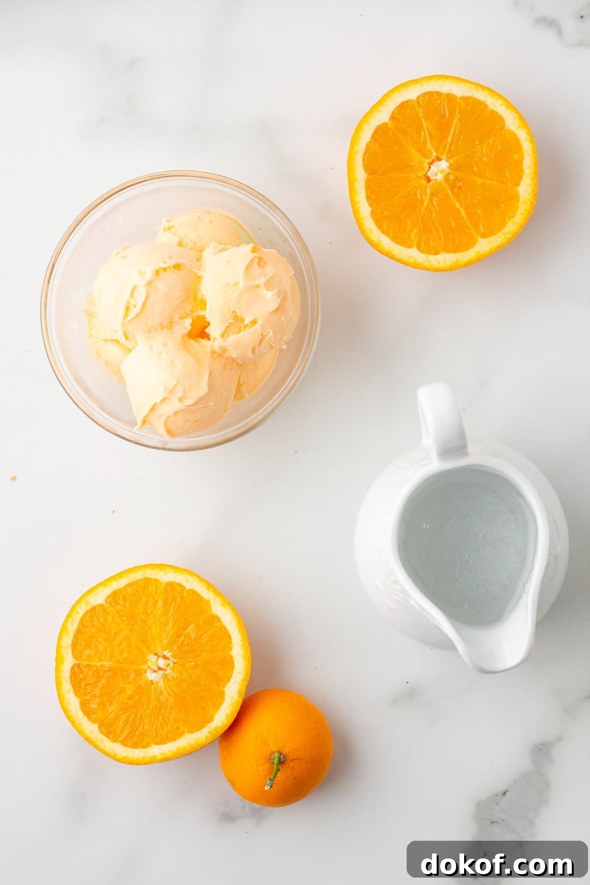 overhead photo of a bowl of orange sherbet, orange halves, and a pitcher of sparkling water