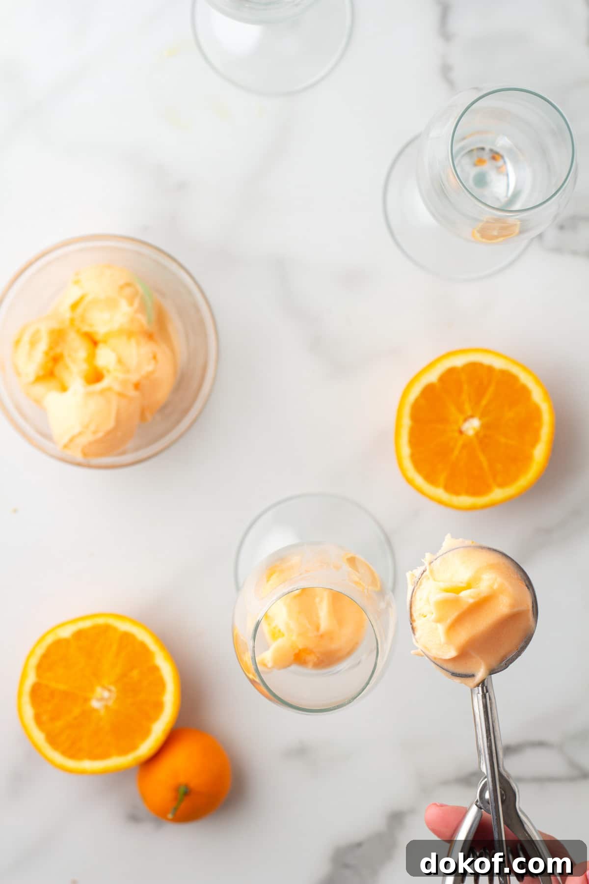 overhead view of scooping orange sherbet into a champagne glass with an ice cream scoop
