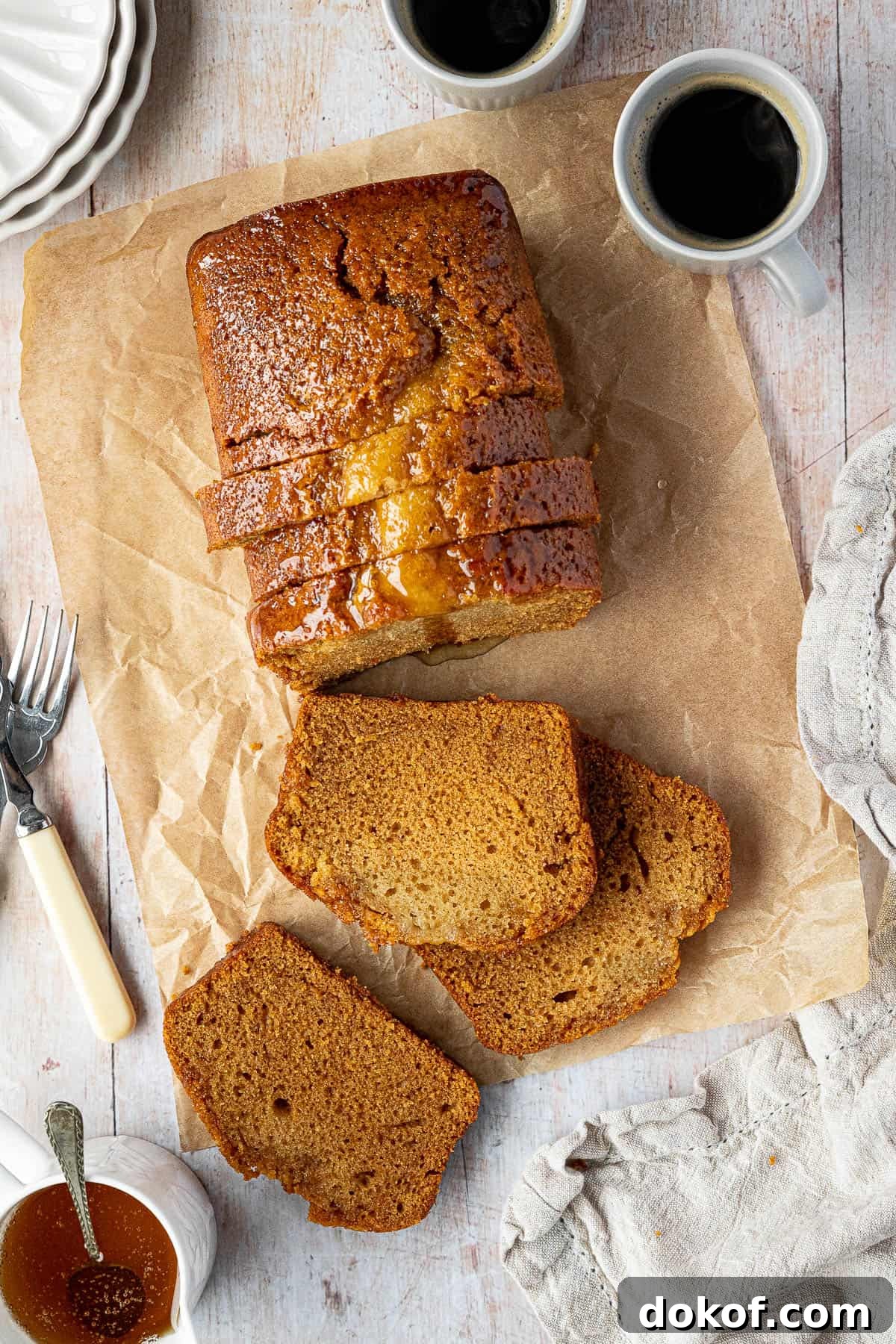 Moist Vegan Golden Syrup Cake Recipe with Sticky Glaze 9 The sliced vegan golden syrup cake on a wooden table with cups of coffee and a jug of golden syrup.