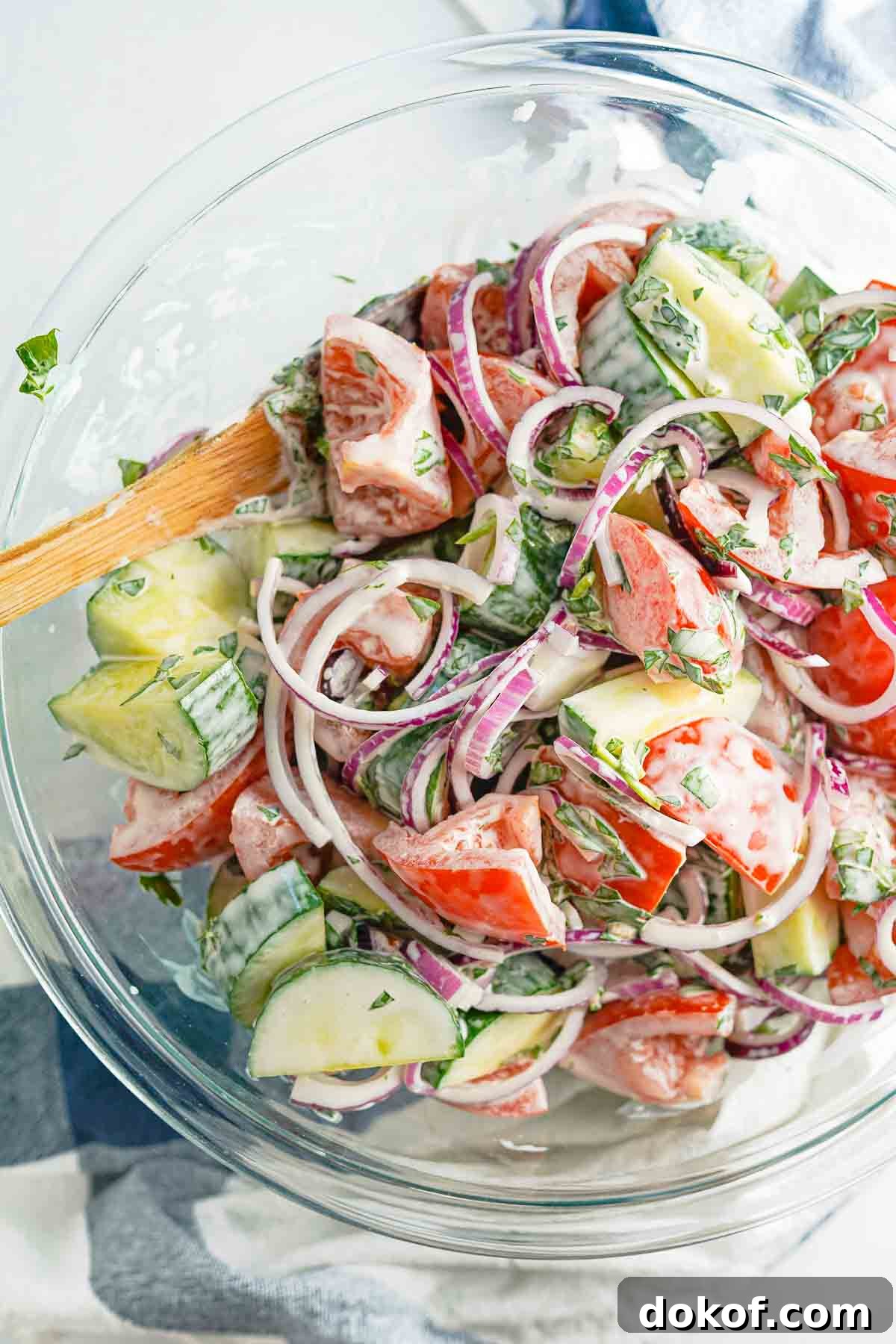 glass bowl with tomato and cucumber salad with wooden spoon in the bowl.