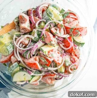 creamy cucumber tomato and onion salad in large glass bowl.