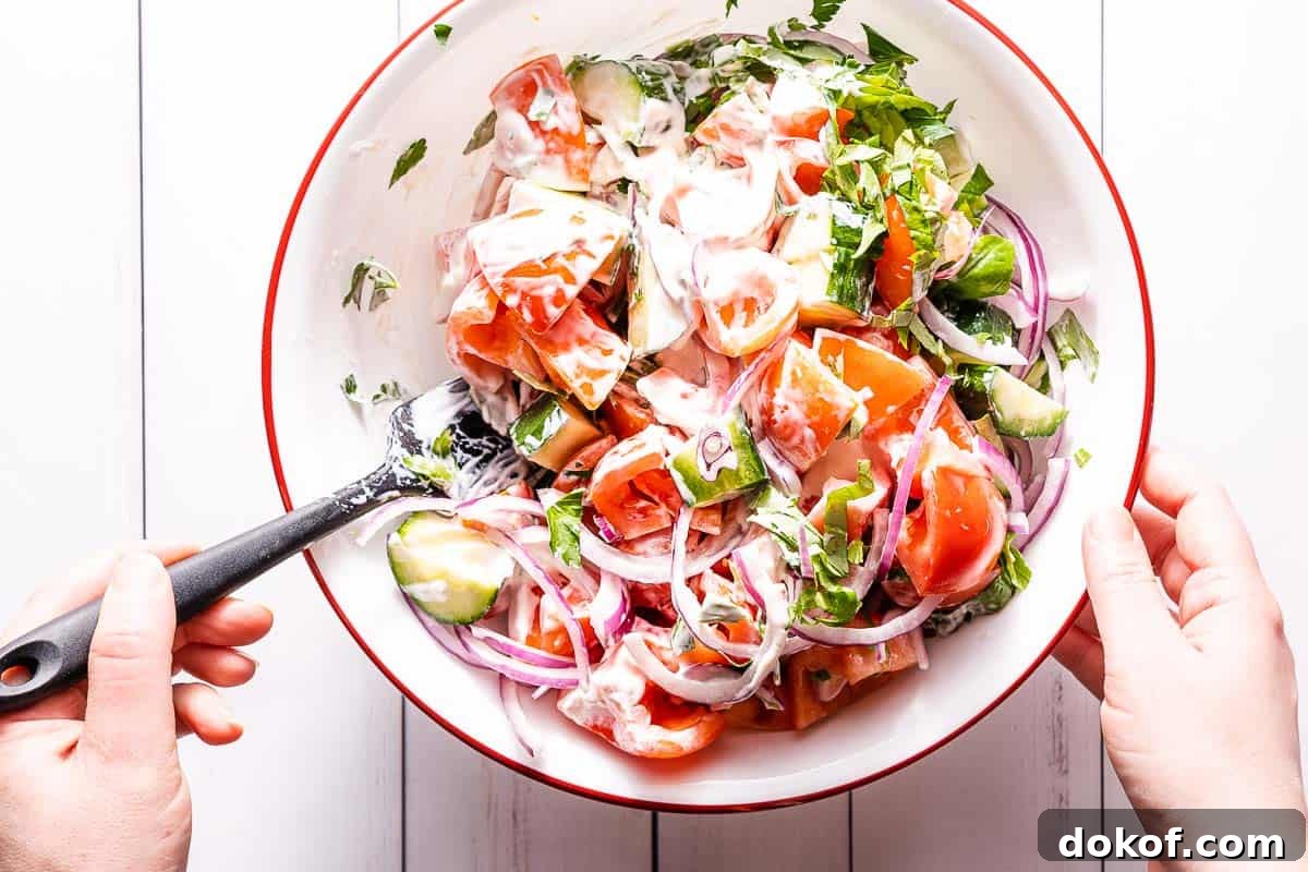 creamy tomato cucumber salad being mixed in large bowl