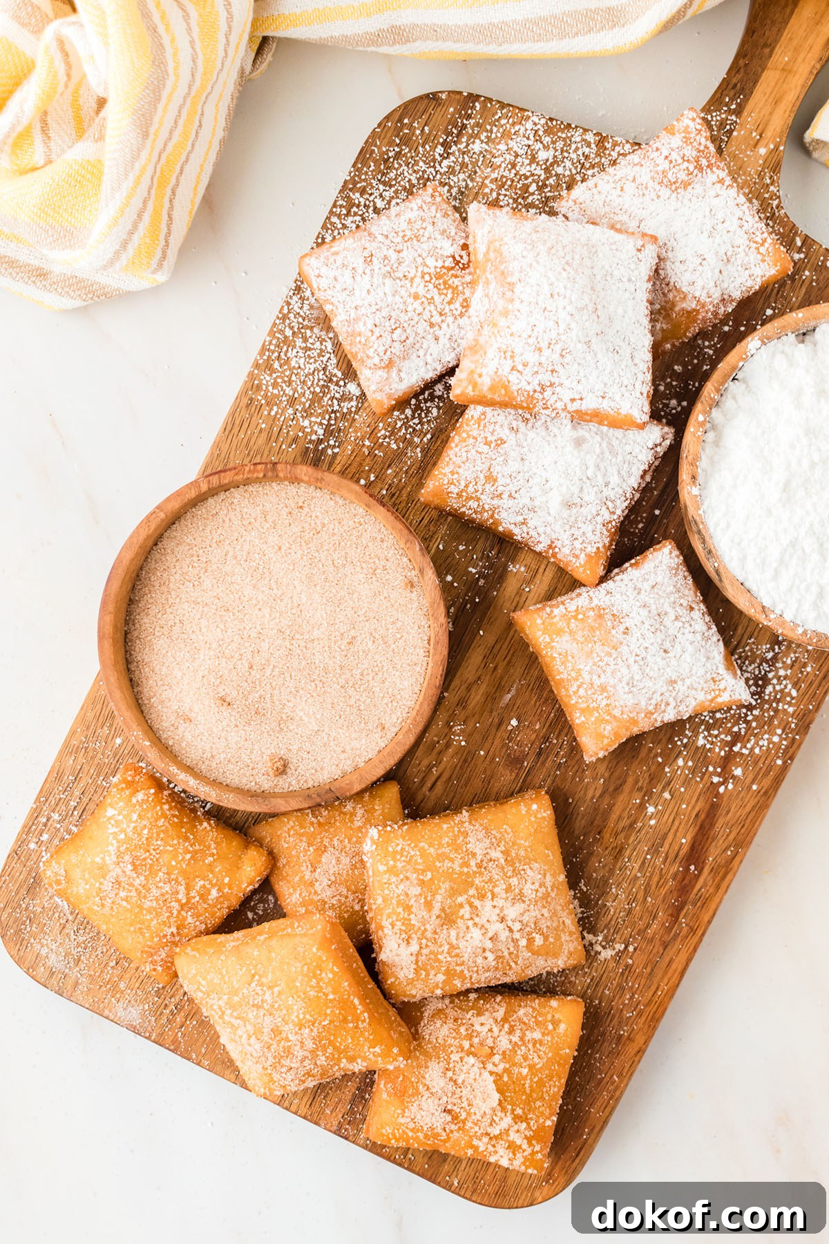 Sopapillas topped with powdered sugar, and sugar-cinnamon served on a wooden serving board. 