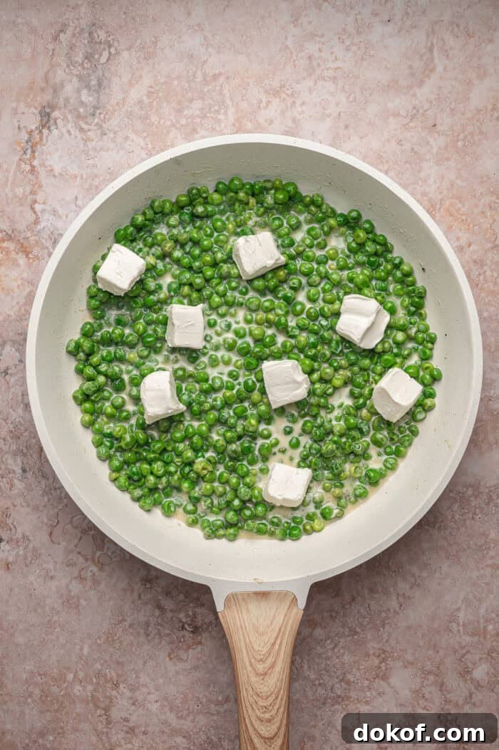 Pats of cream cheese on top of peas in a skillet