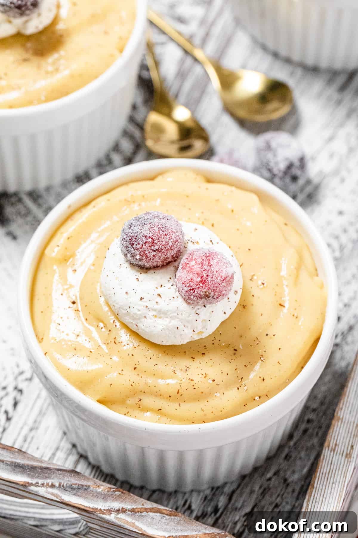 Creamy Homemade Eggnog Pudding Recipe for the Holidays 4 close up of pudding topped with whipped cream and sugared cranberries with gold spoons in the background