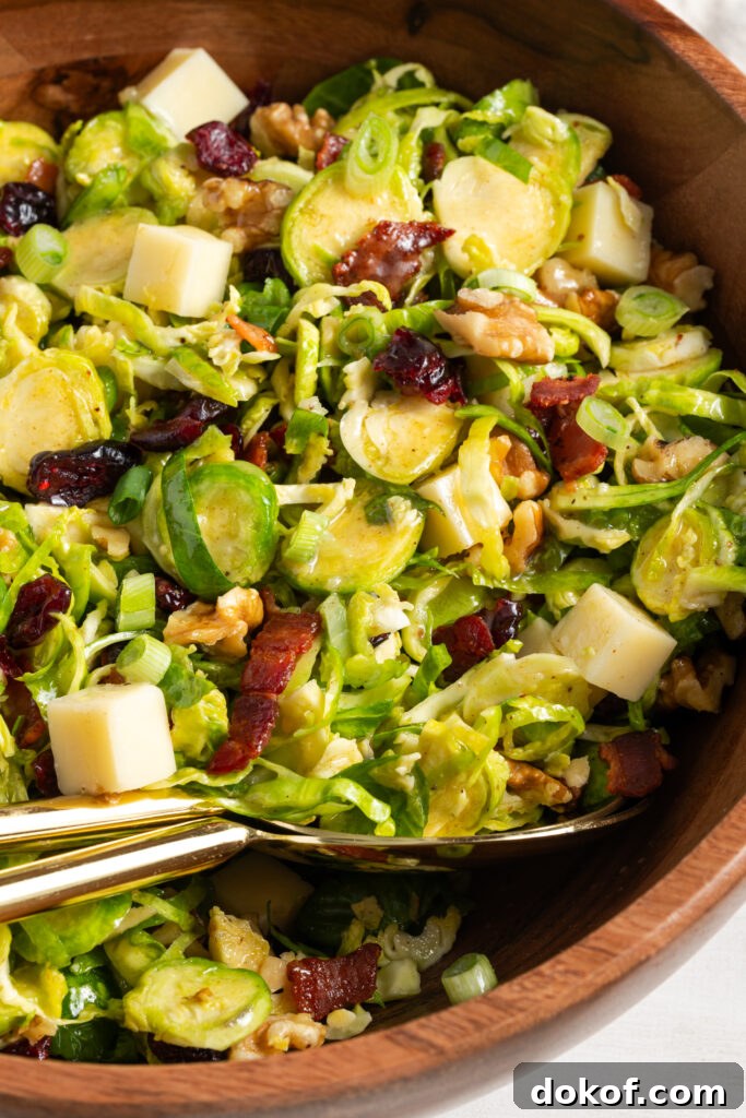 Citrus-Shaved Brussels Sprout Salad with Toasted Almonds 3 closeup of shaved brussel sprout salad in a wooden serving bowl with gold serving spoons.