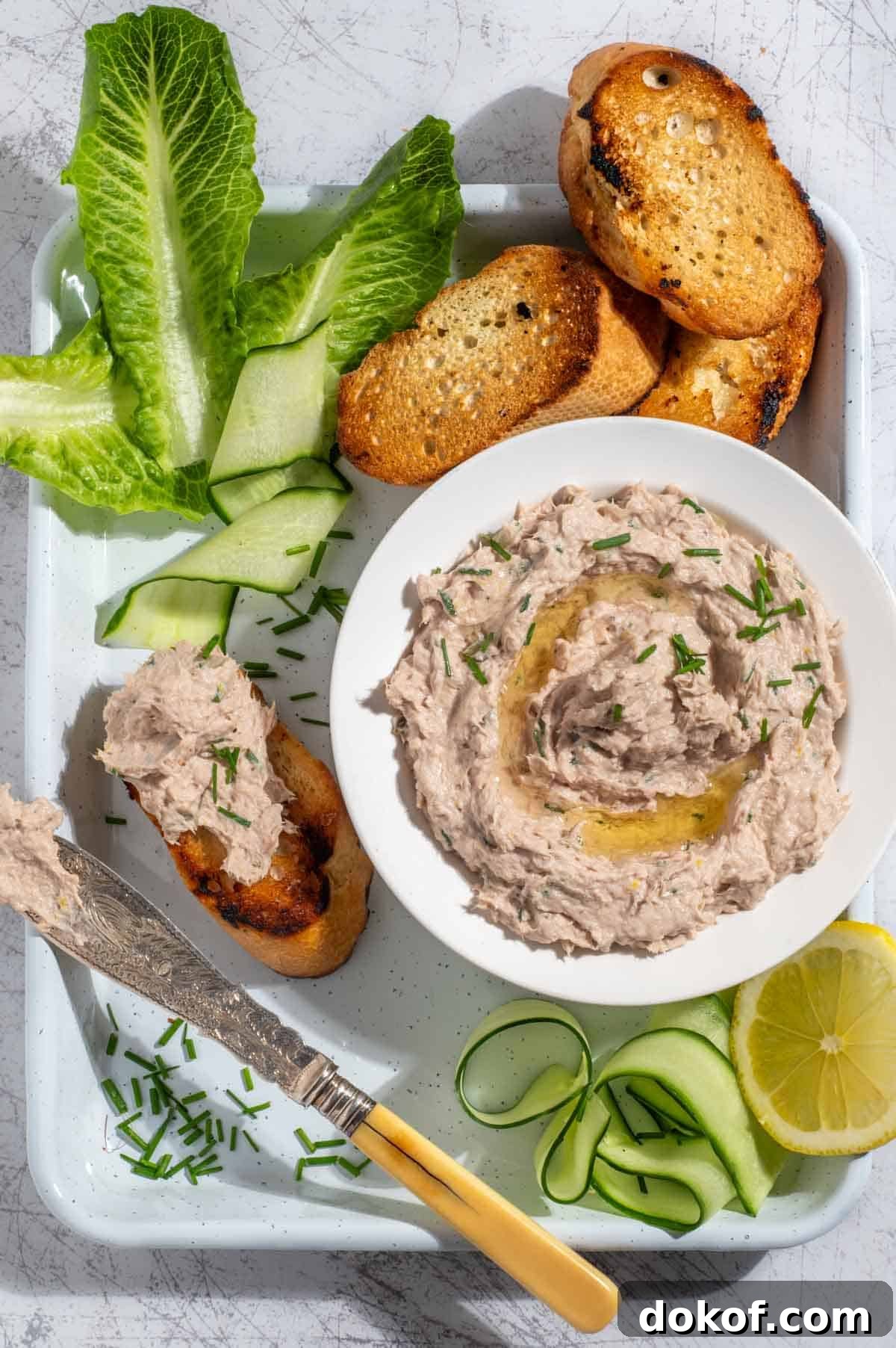A bowl of tuna pate surrounded by toasted baguette, cucumber ribbons and lettuce. 