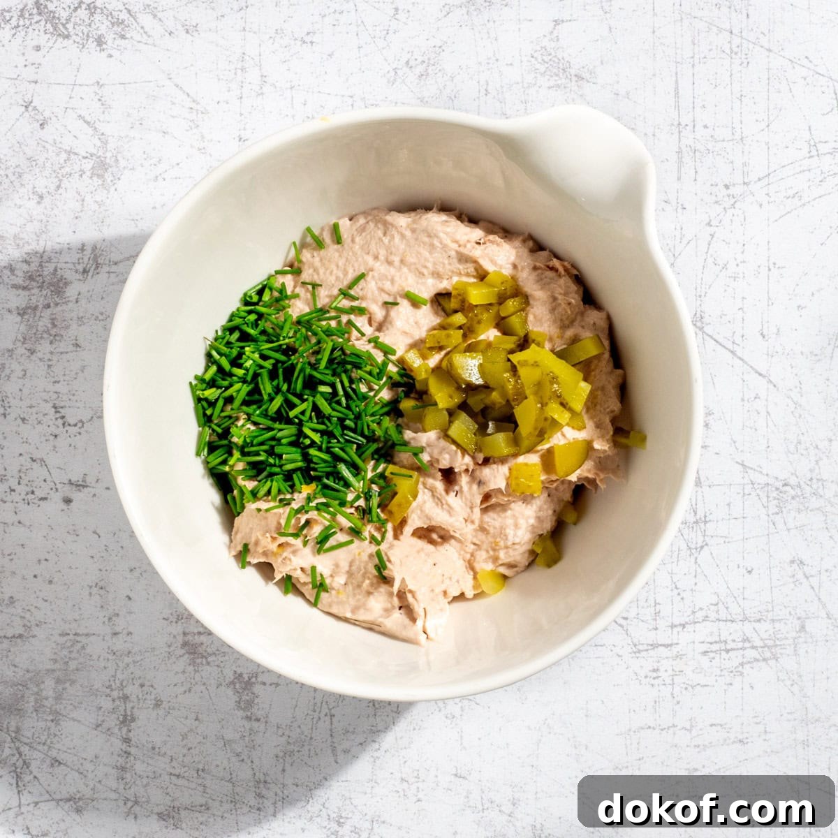 Blended tuna pate in a white bowl with chopped chives and gherkins.