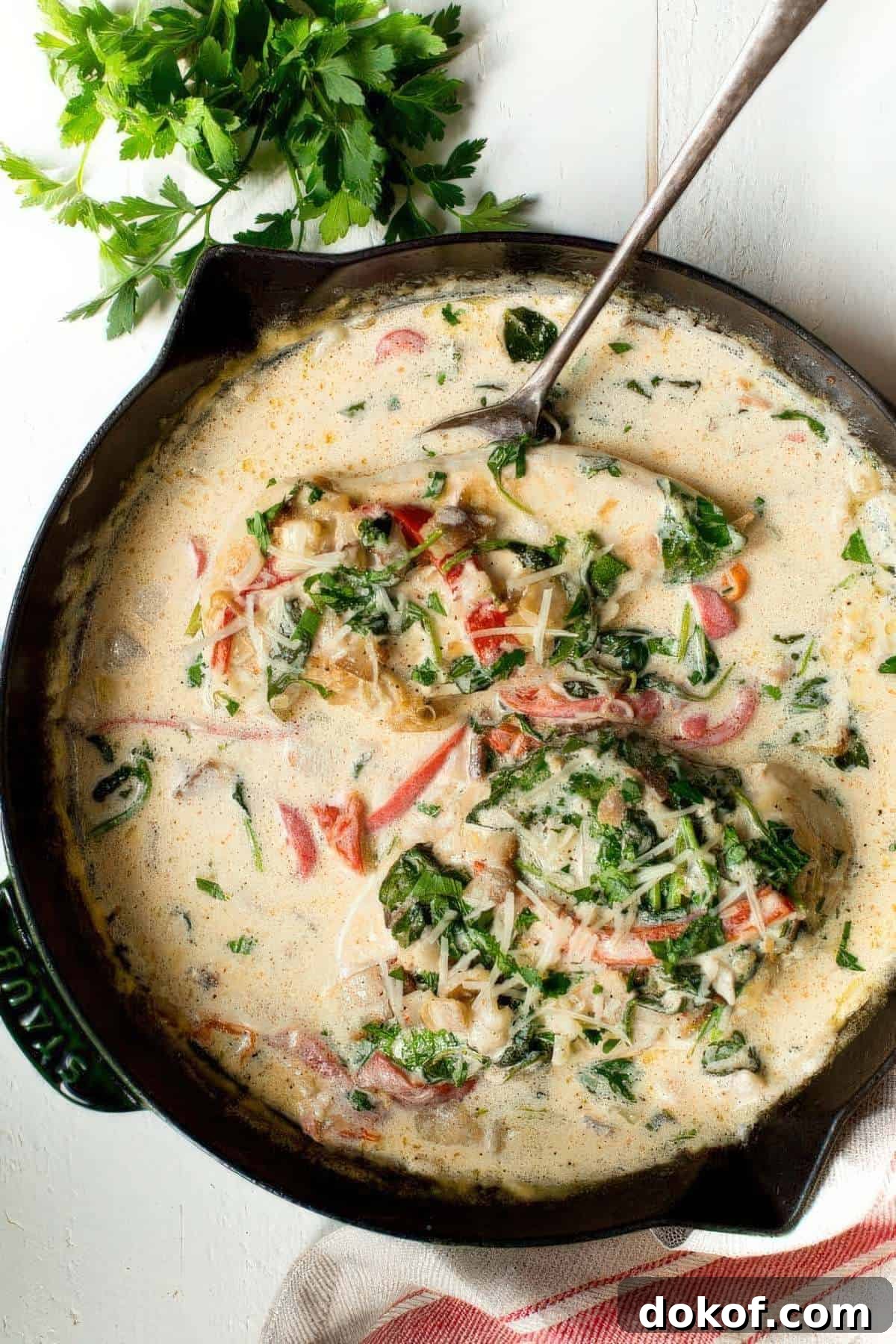 Overhead view of creamy chicken bacon skillet with spinach and roasted red peppers in a cast iron pan