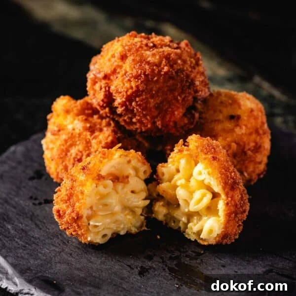 A black platter piled with mac and cheese bites. One is broken open, revealing the creamy mac inside.