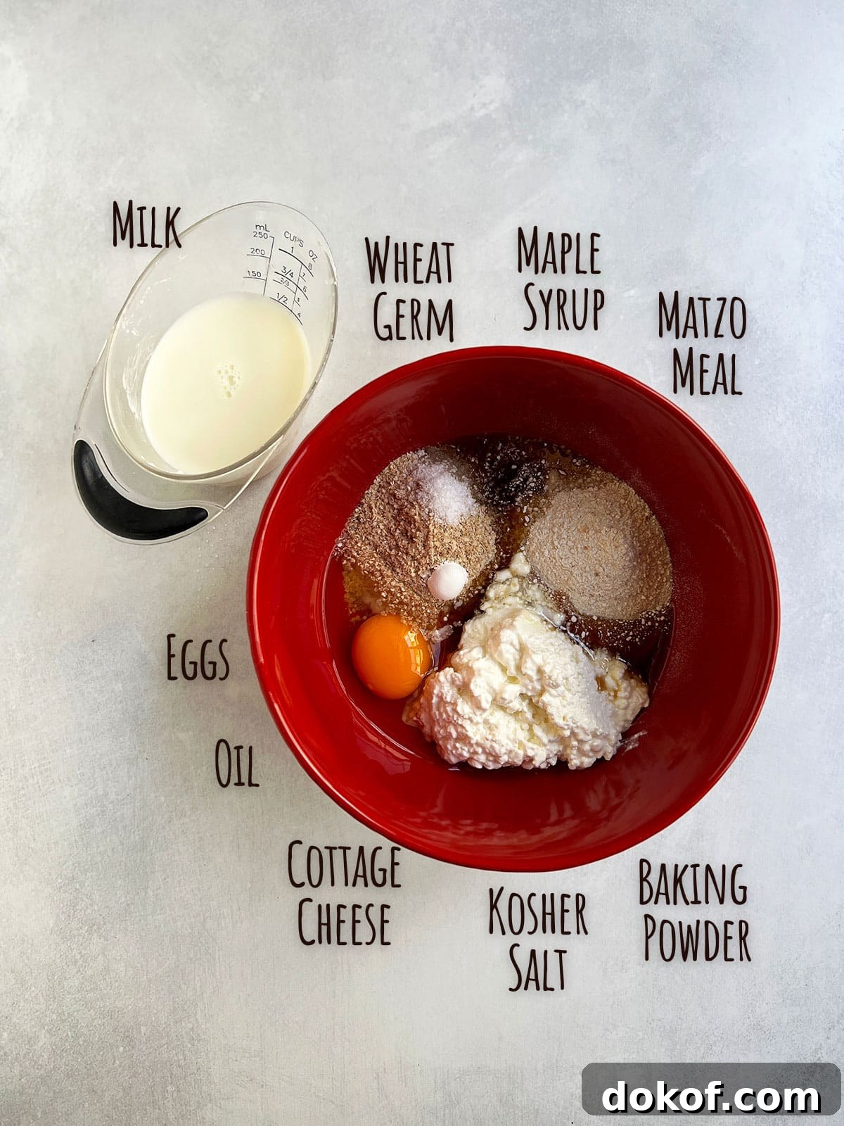 Ingredient shot with all pancake ingredients in a red bowl except for the milk which is in a measuring cup.