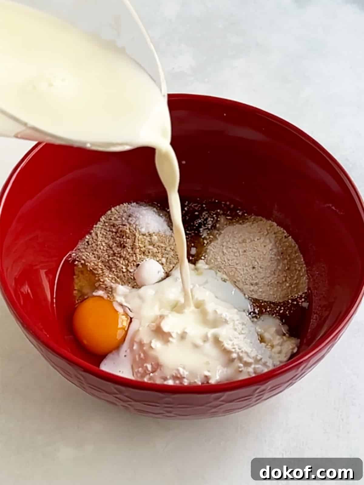 Milk pouring into a red bowl that contains all of the cottage cheese pancake ingredients.