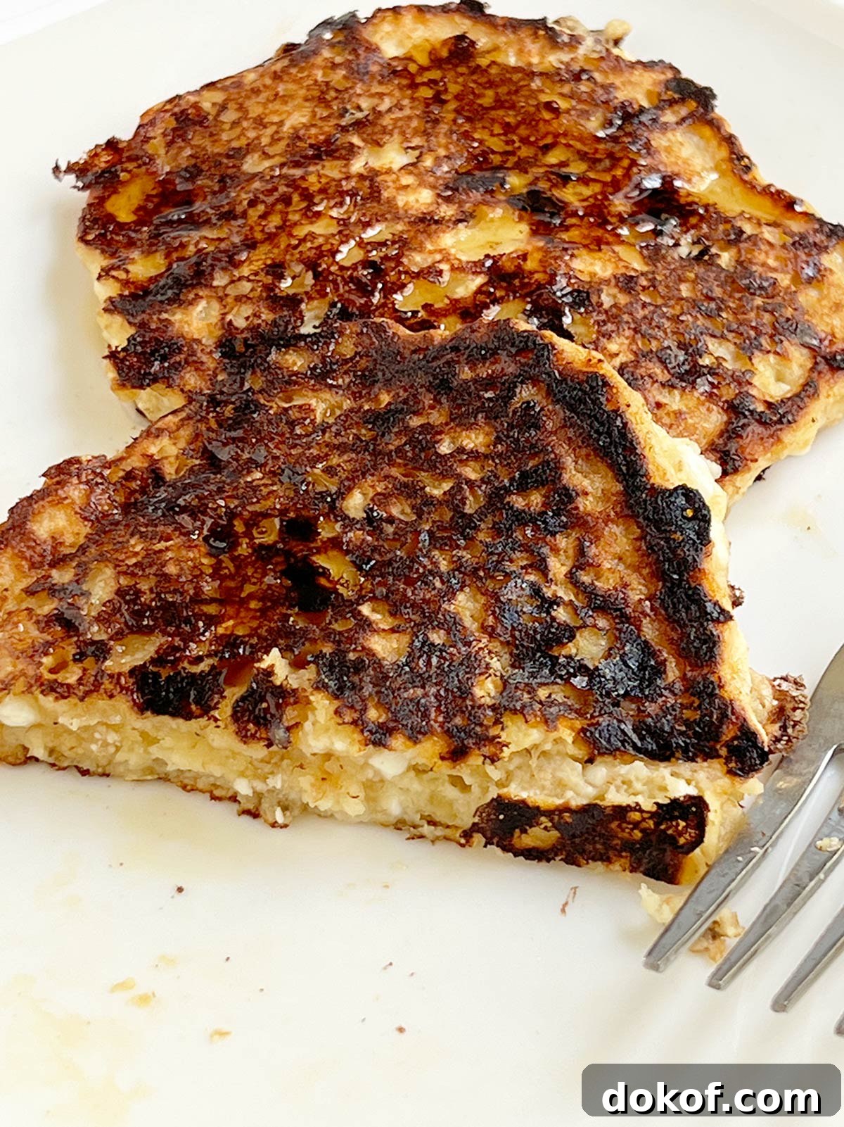 Cheese latke cut open with a fork on the side on a white plate.