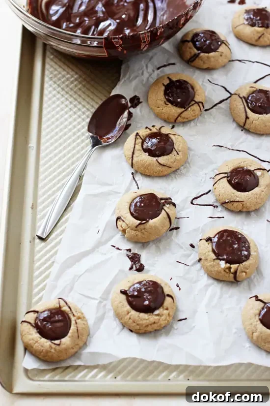 Chocolate Peanut Butter Thumbprint Cookies on a baking sheet with a bowl of melted chocolate.