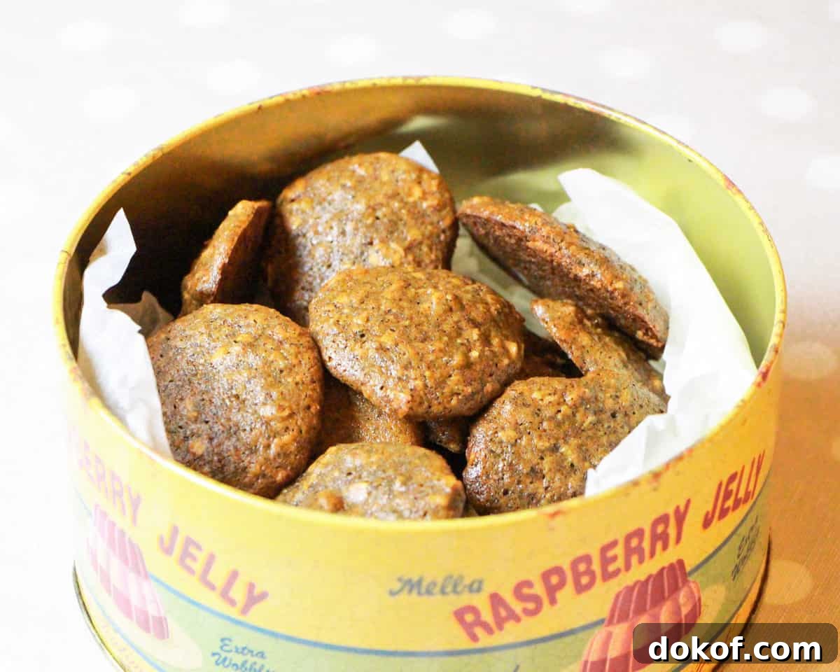 an old-fashioned cake tin filled with Zesty Orange and Walnut Cookies on a spotty taupe and white tablecloth.