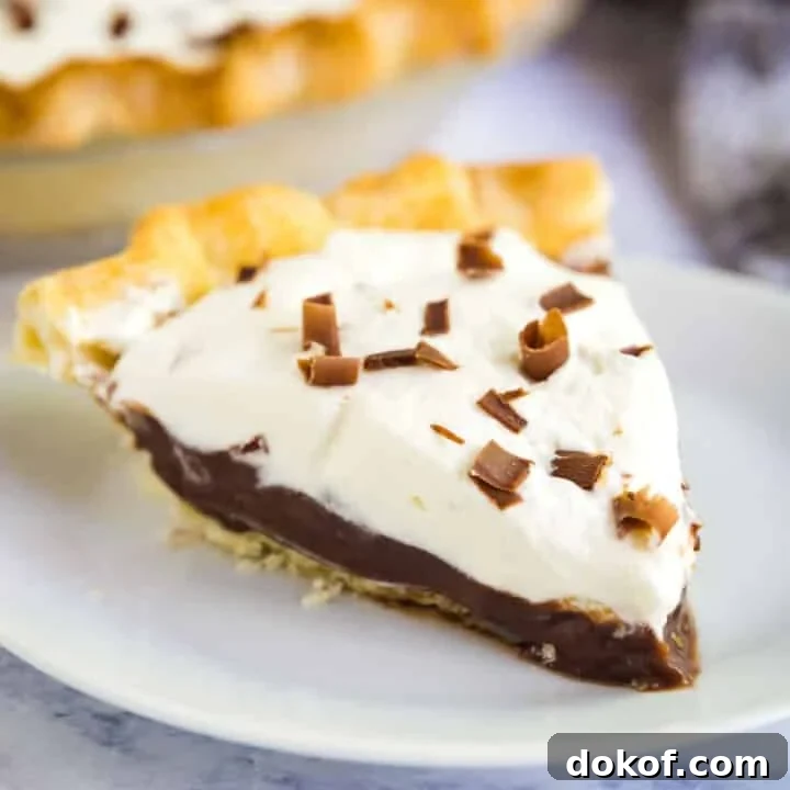 A close up image of a slice of chocolate pudding pie on a white plate with the rest of the pie behind it.