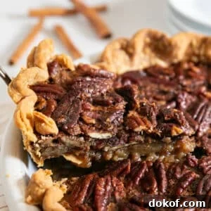A slice of pecan pie being pulled from the pie with plates and cinnamon sticks in the background.