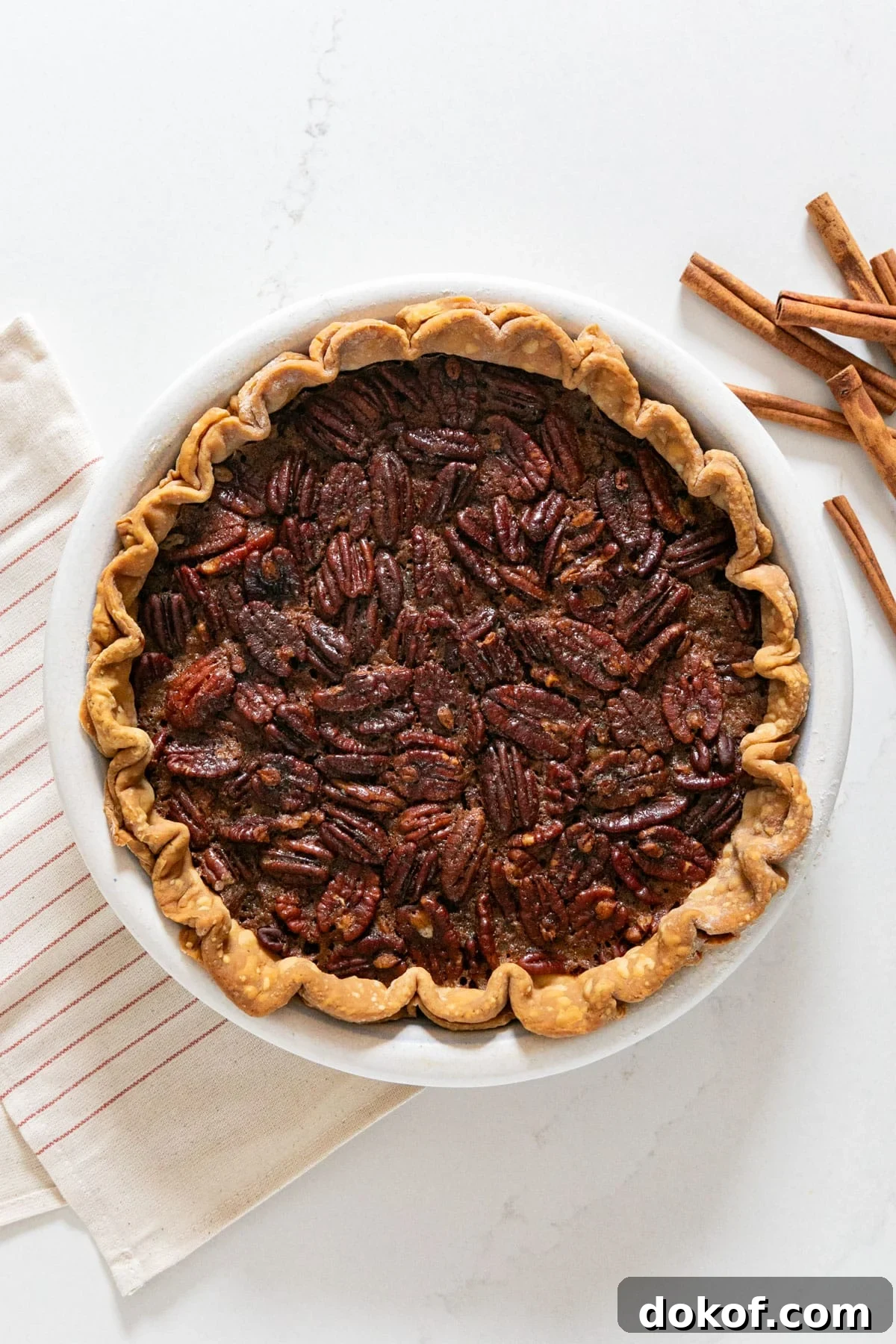 An overhead image of a pecan pie with a striped napkin and cinnamon sticks next to it.