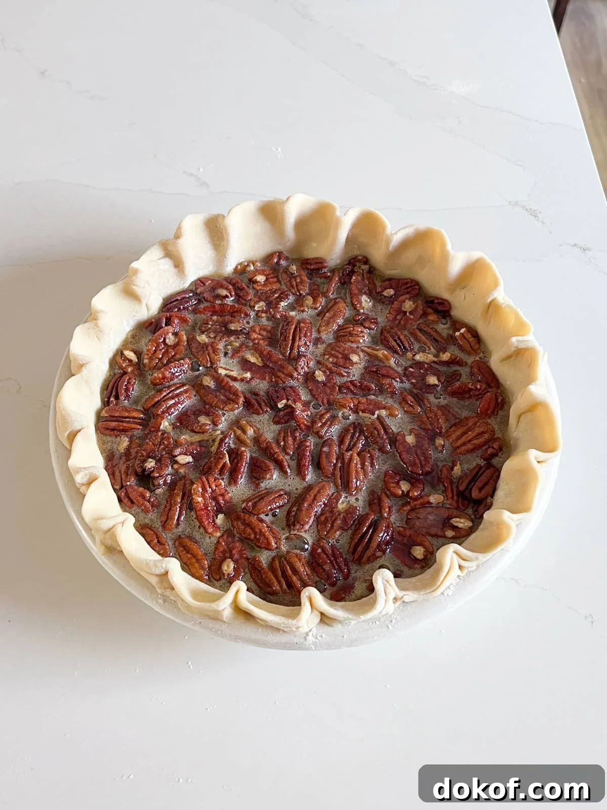 Raw pie crust with pecans and filling in it.