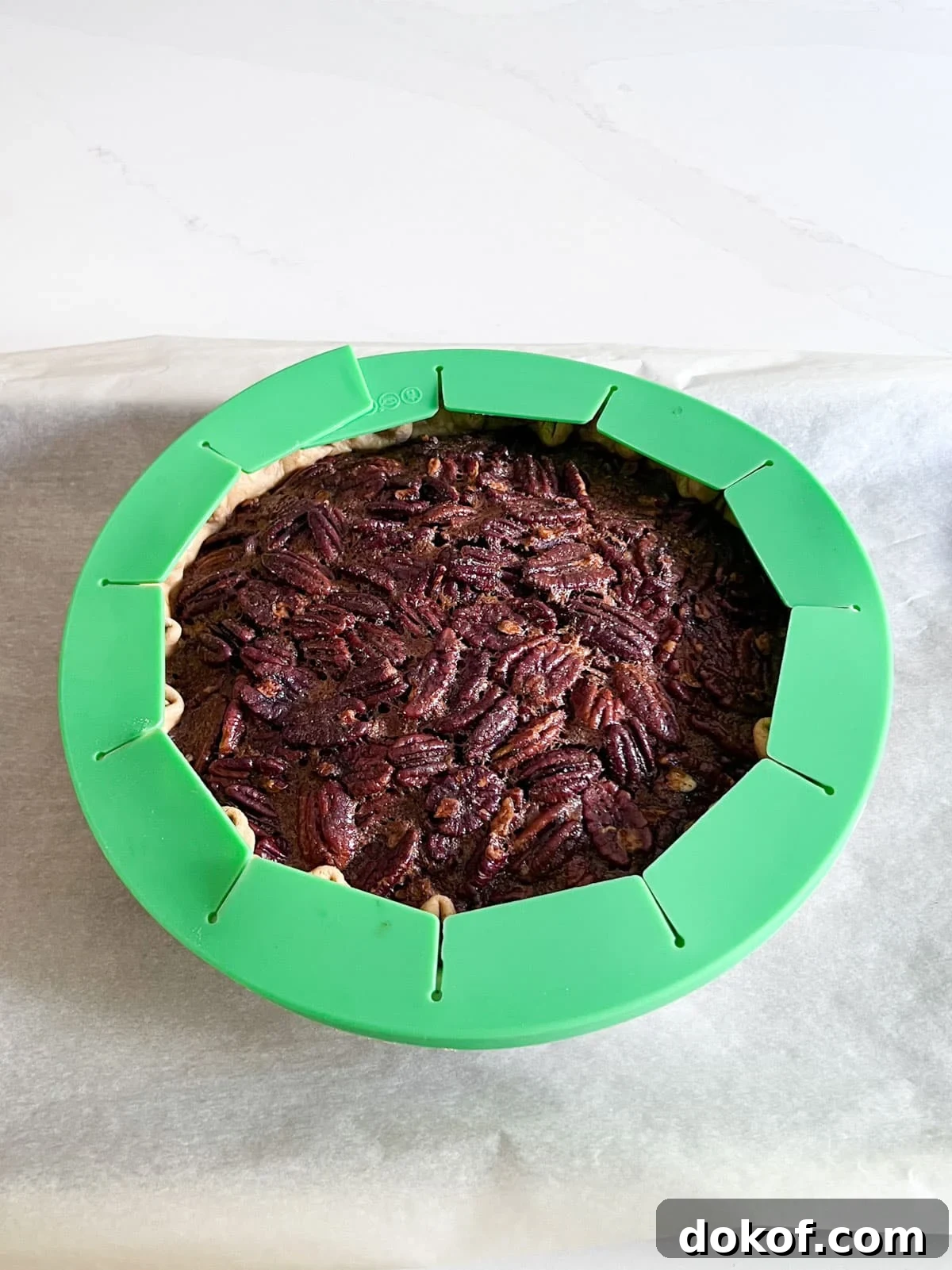 A partially baked pie with a green pie shield over the outer crust.
