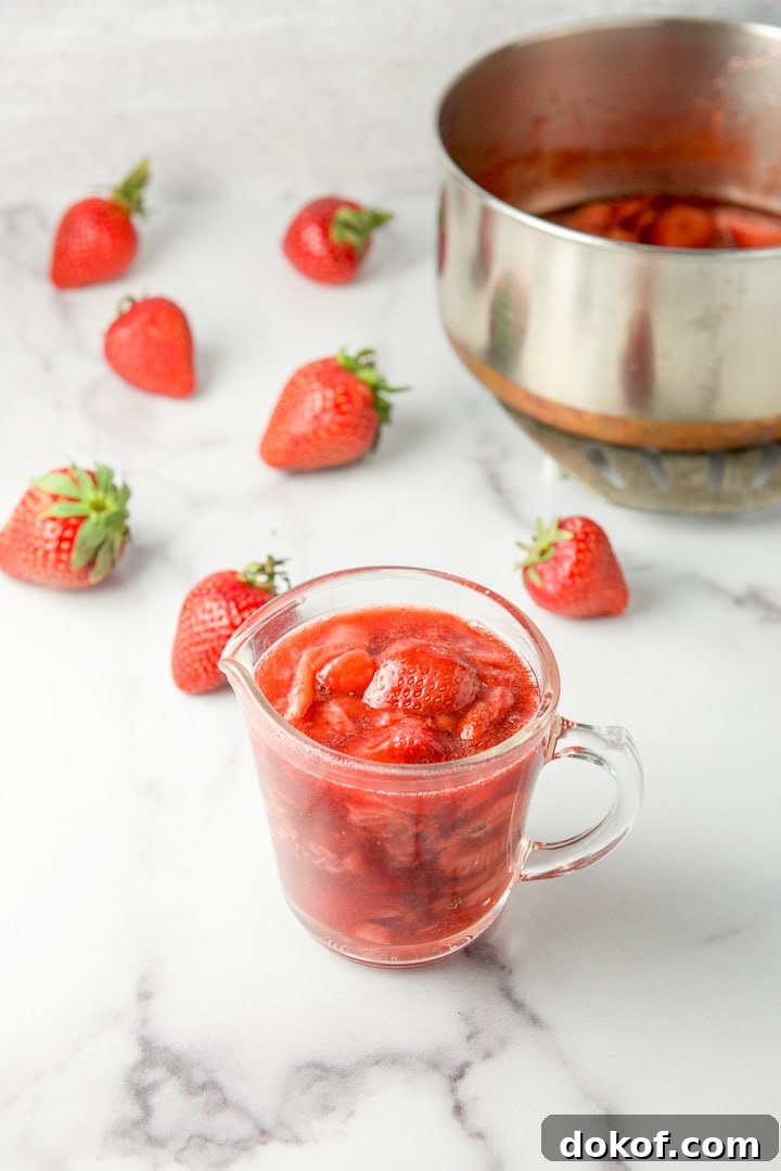 Some of the sauce in a glass pitcher with strawberries in the background