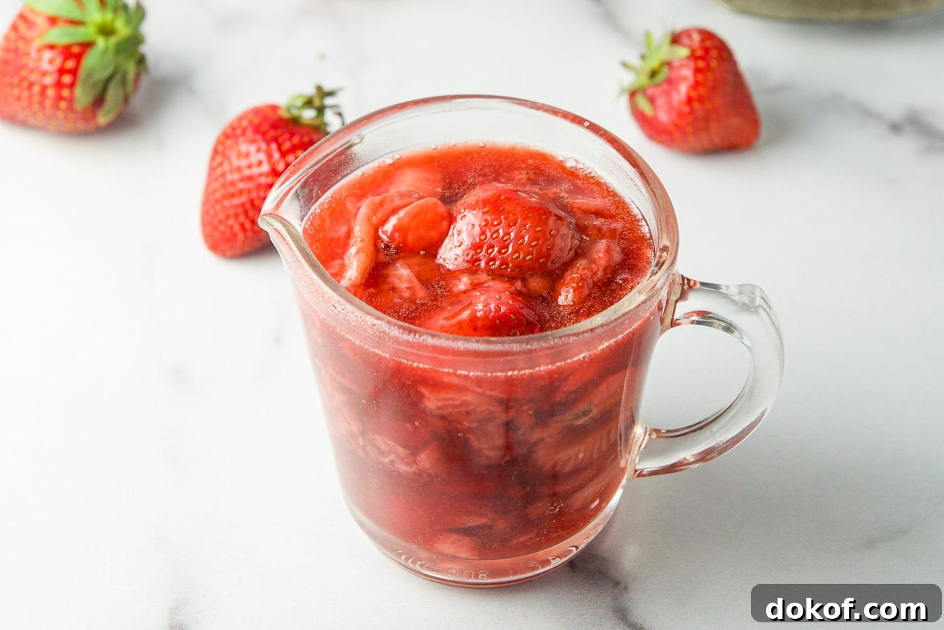 A small glass jar filled with strawberry sauce with strawberries on the table