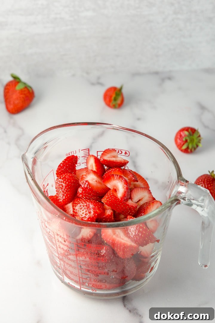 Strawberries cut up in a glass measuring cup with a few berries in the background