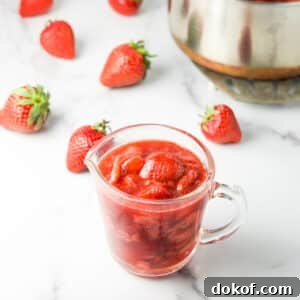Some of the sauce in a glass pitcher with strawberries in the background