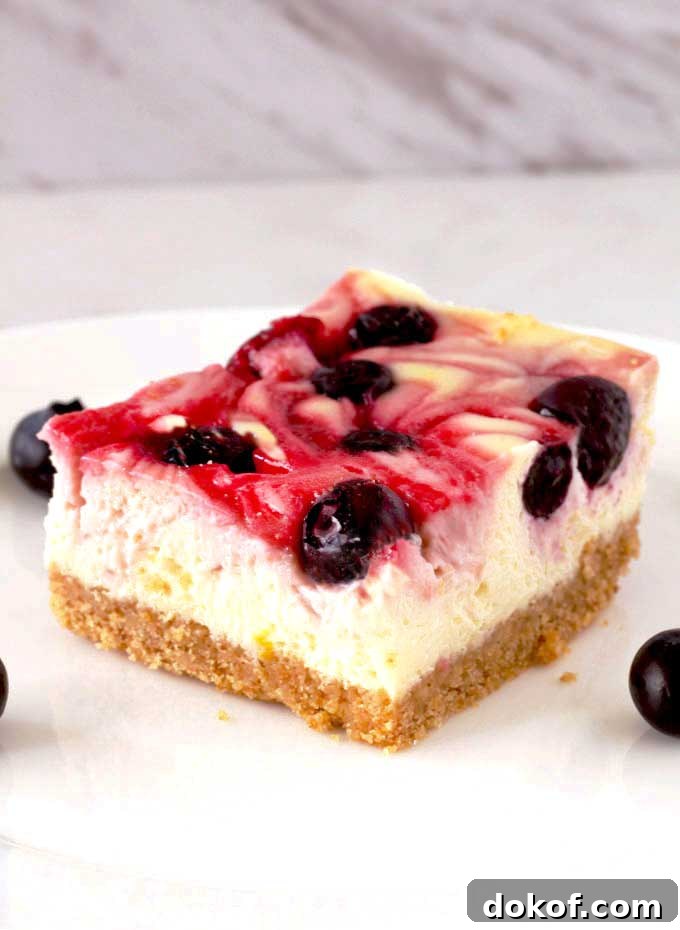Berry Swirl Cheesecake Bars — Luscious No-Bake Dessert Recipe 3 A berry swirl cheese cake bar on a white surface