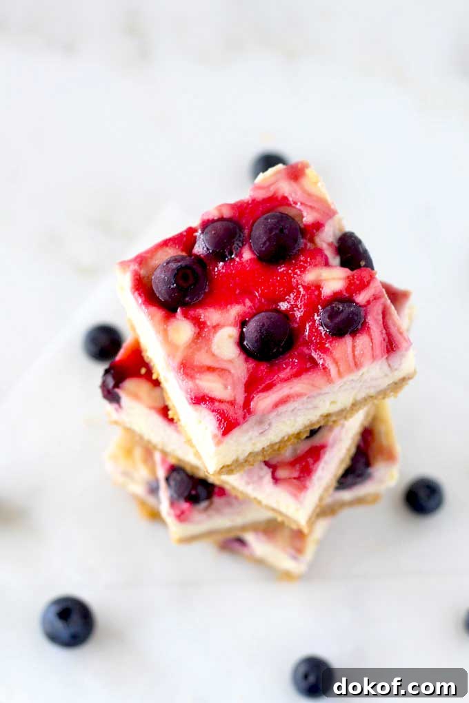 Berry Swirl Cheesecake Bars — Luscious No-Bake Dessert Recipe 4 Top view of a stack of cheesecake bars with blueberries and raspberry swirl.