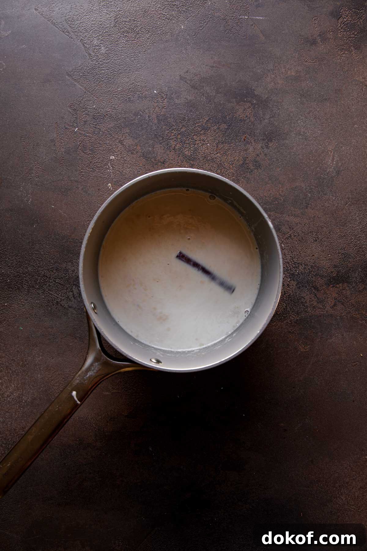 A sauce pan with milk and a cinnamon stick.
