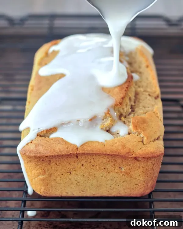 a full loaf of snickerdoodle bread on a wire rack, white icing is being poured over top