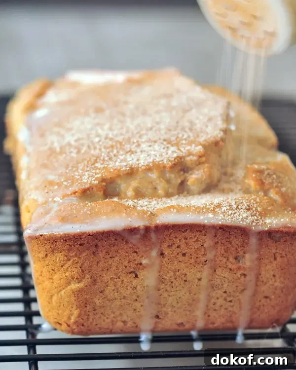 a full loaf of snickerdoodle bread on a wire rack, being sprinkled with cinnamon
