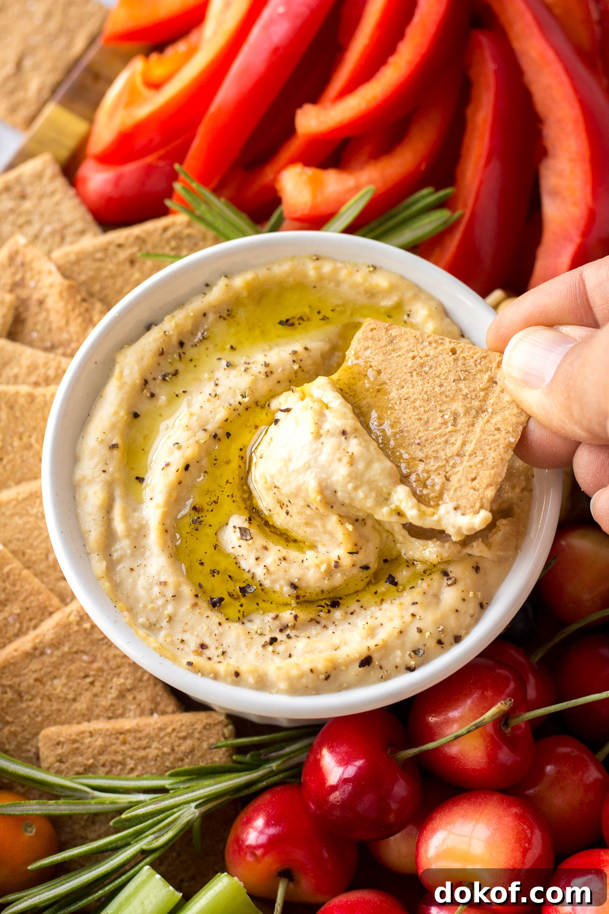 hand dipping cracker into hummus from Vegan Cheese Board by Flora & Vino