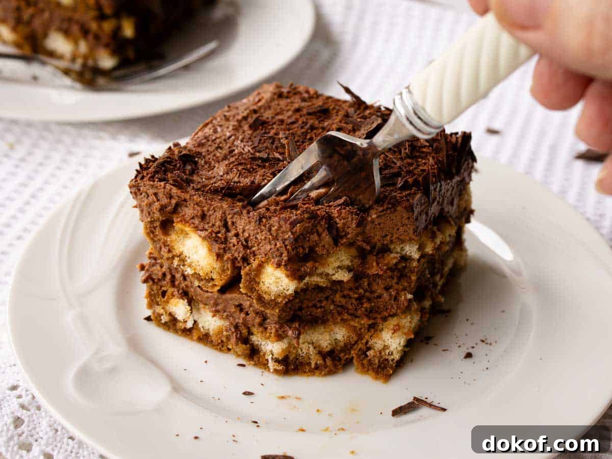 Decadent Chocolate Tiramisu Recipe for Coffee Lovers 13 Square of tiramisu with chocolate on a white plate with a fork plunged in.