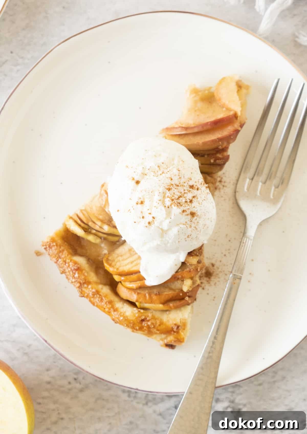 Rustic Apple Galette Recipe: Simple Homemade Apple Tart 11 A slice of apple tart with cream on a white plate. A silver fork. Grey surface.