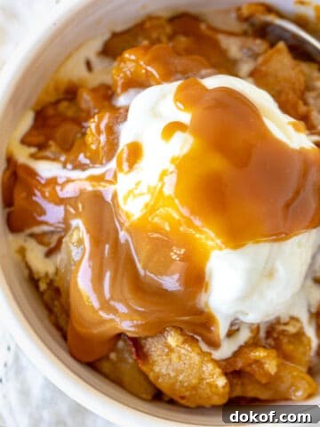 Caramel topped ice cream scoop over apple dump cake in white bowl, white napkin.