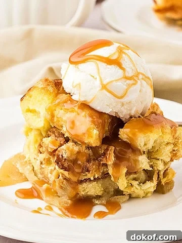 Serving of apple bread pudding with cream and caramel on a white plate.