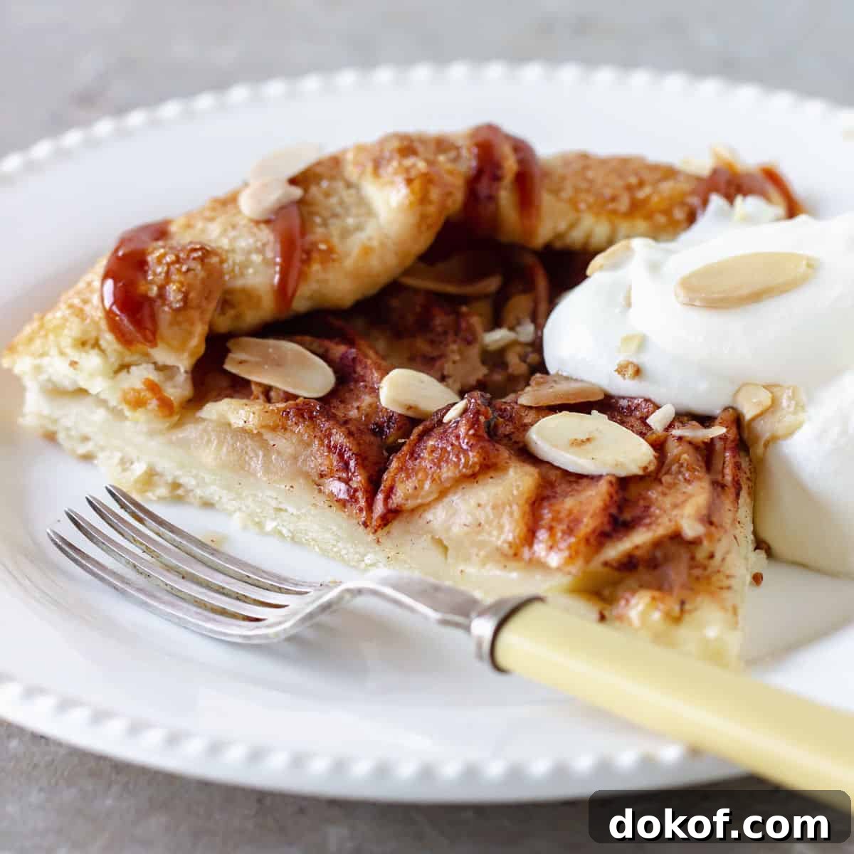 Rustic Apple Galette Recipe: Simple Homemade Apple Tart 18 Single slice of apple tart with cream on a white plate with fork.