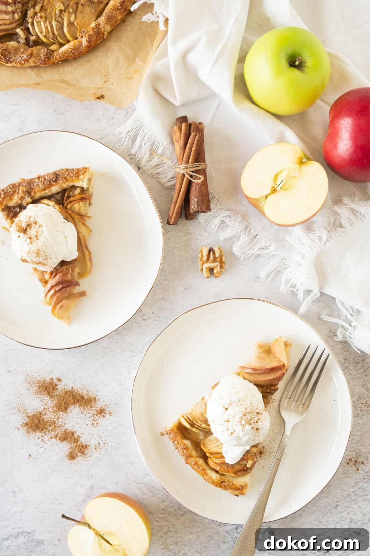 Rustic Apple Galette Recipe: Simple Homemade Apple Tart 4 Two white plates with apple galette and cream. Grey surface, fresh apples, cinnamon sticks, walnuts.