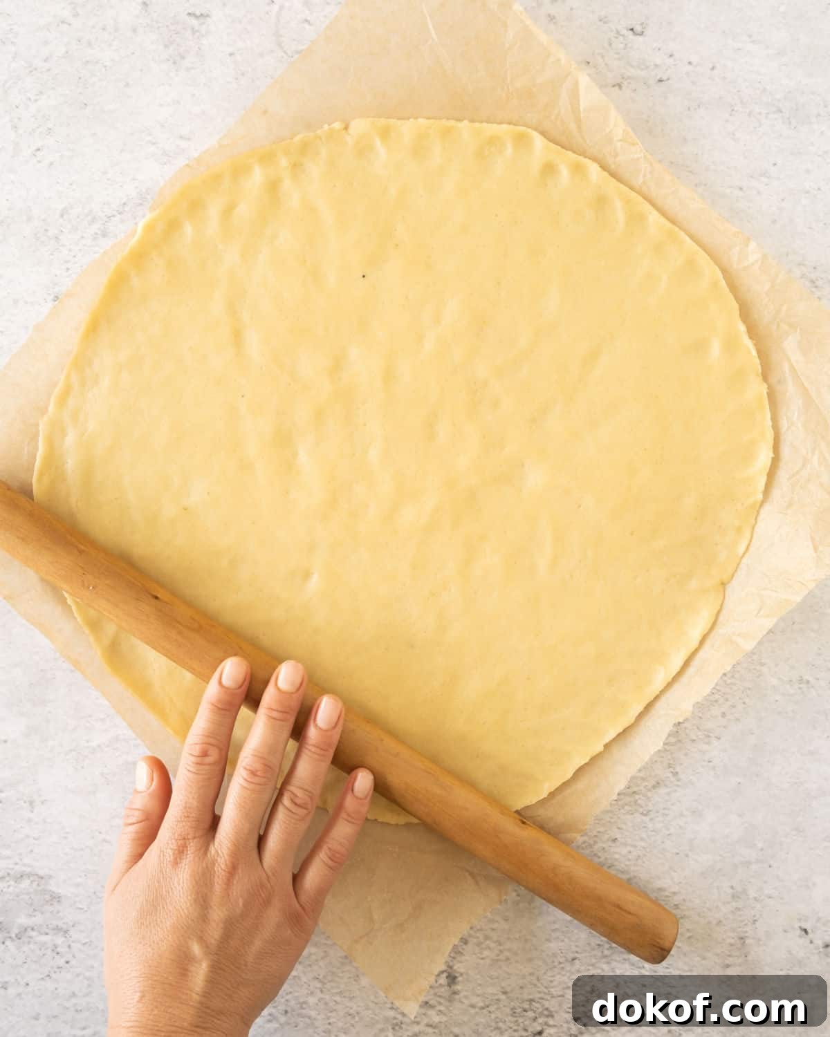 Rustic Apple Galette Recipe: Simple Homemade Apple Tart 6 Rolled galette dough on parchment paper and light grey surfce. Hand holding rolling pin.