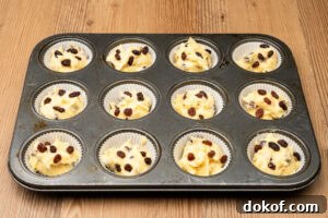 Twelve cupcake cases filled with cake mixture in cupcake tray