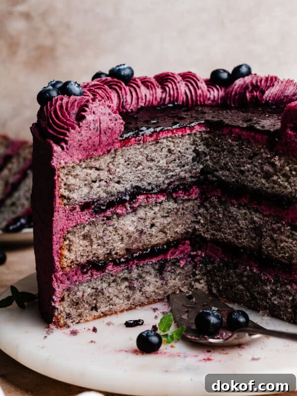 The sliced blueberry cake on a cake plate, with stunning layers of blueberry cake, blueberry filling, and blueberry frosting.