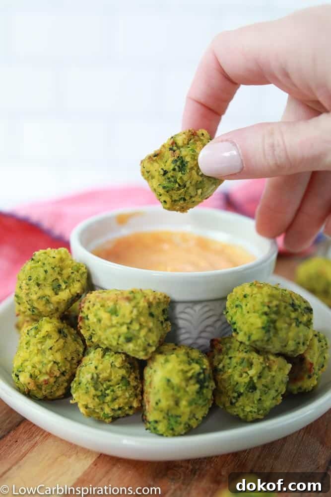 baked broccoli bites a white plate with a white bowl of dipping sauce and a handing holding one close up