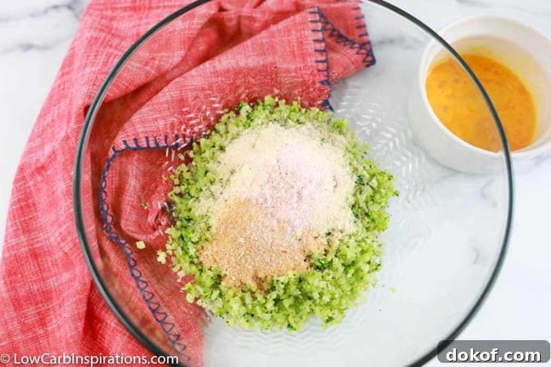 keto broccoli tots ingredients in a clear bowl on a table with a pink towel on the side 